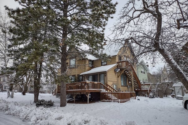 Rustic log cabin interior with wooden staircase, dining table, and kitchen with stainless steel appliances